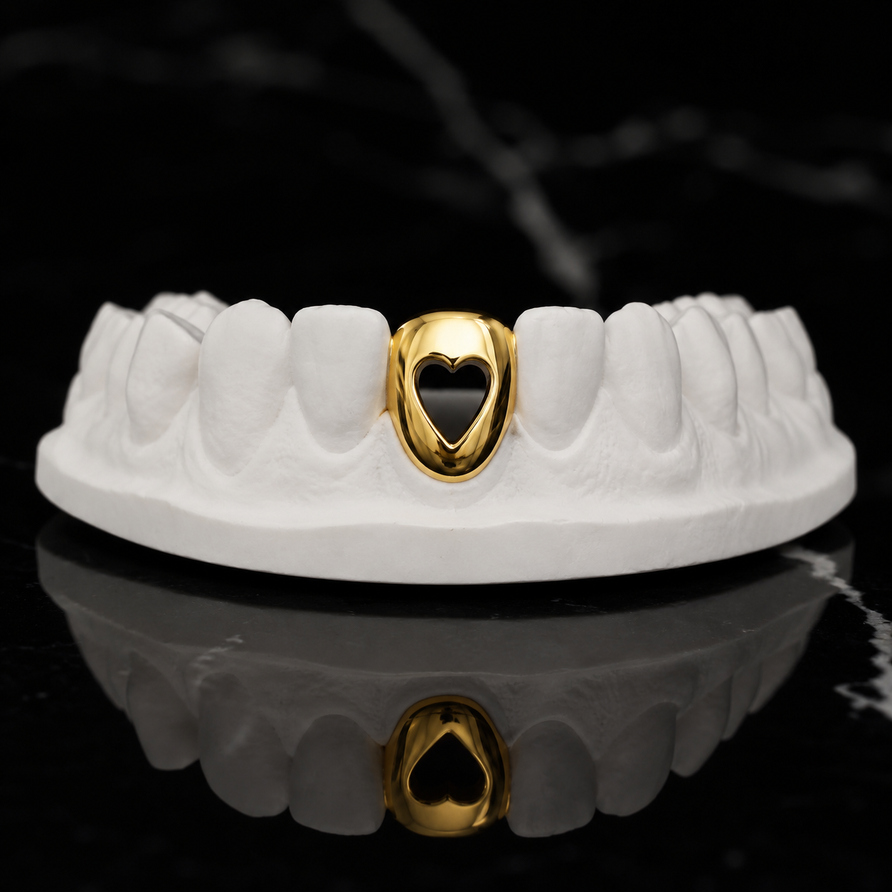 Custom solid yellow gold heart-shaped open-face gap filler grill handcrafted with a mirror-polished finish and displayed on a white dental mold for a luxury jewelry product photograph.